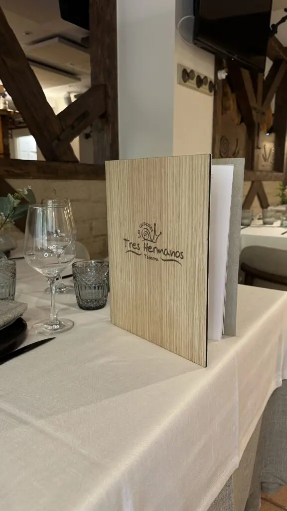 Carta de madera con el logotipo de Tres Hermanos grabado, sobre una mesa de restaurante